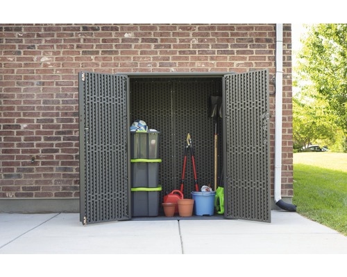 Offener Geräteschuppen aus Kunststoff mit Gartengeräten vor einer Backsteinmauer