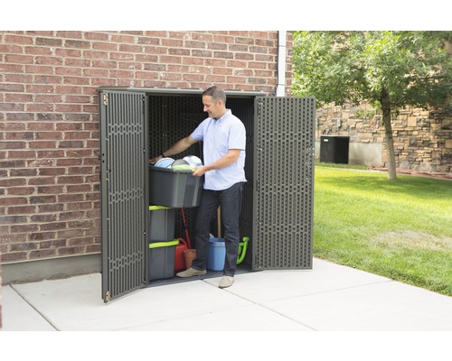 Mann verstaut Gartengeräte in einem Geräteschrank aus Kunststoff vor einer Ziegelmauer