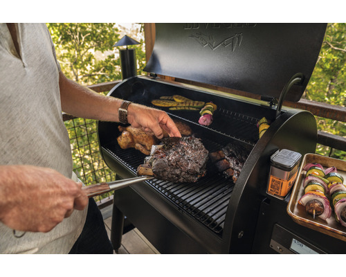 Mann grilliert Fleisch und Gemüse auf einem Grill im Freien.