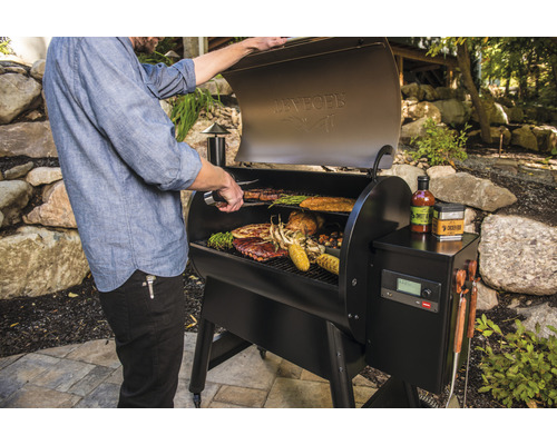 Ein Mann grilliert Steaks, Rippchen, Hähnchen, Mais und Gemüse auf einem schwarzen Grill im Freien.