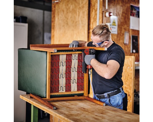 Mann befestigt Polsterbezug mit Tacker an Stuhl