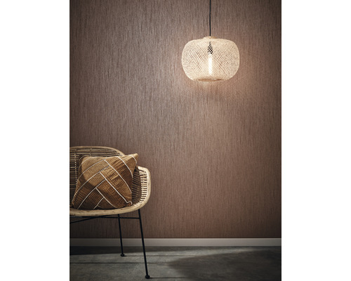 Raumszene mit strukturierten Tapeten, Rattansessel, Kissen und Pendelleuchte
