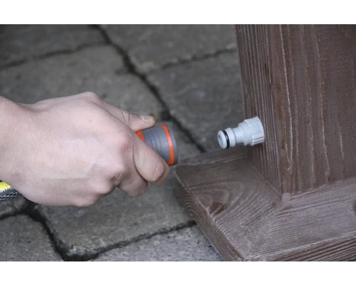 Anschliessen eines Gartenschlauchs an einen Wasserhahn an einem Holzbalken