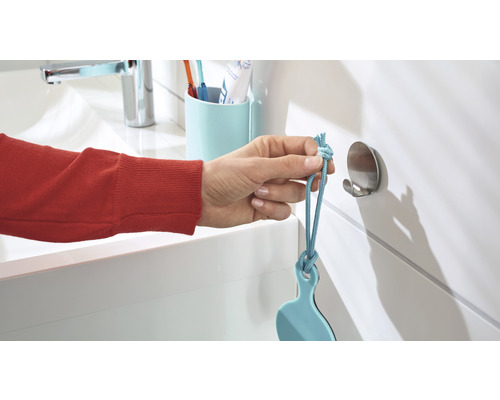 Une main accroche une raclette de douche bleue à un crochet mural dans la salle de bains.