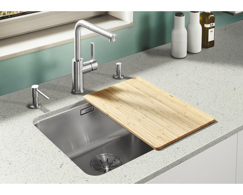 Küchenspüle aus Edelstahl mit Armatur, Spülmittelspender und Schneidebrett aus Bambus auf einer Arbeitsplatte.