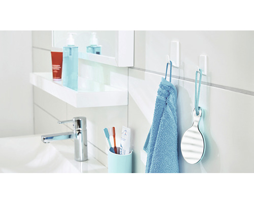 Lavabo de salle de bain avec robinet, serviette, miroir à main et crochets autocollants.