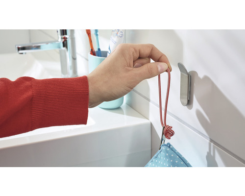 Eine Hand hängt einen Beutel an einem Edelstahl-Wandhaken im Badezimmer auf.