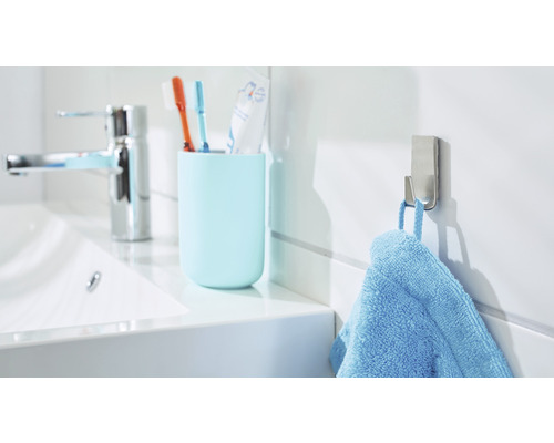 Salle de bains lumineuse avec lavabo, gobelet pour brosses à dents, patère et serviette bleue
