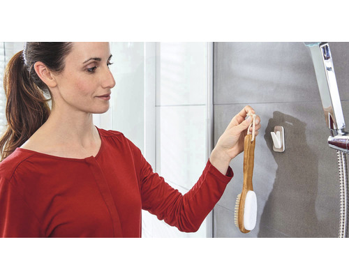 Frau hängt Badebürste mit Klebehaken in Badezimmer auf