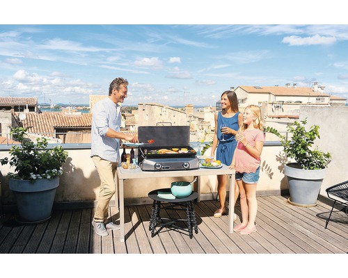 Une famille fait des grillades sur un toit-terrasse avec un barbecue à gaz et une table d''appoint par beau temps.