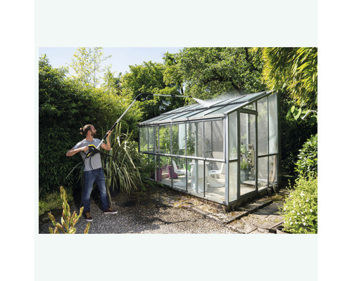 Homme nettoie serre avec un nettoyeur haute pression dans le jardin.