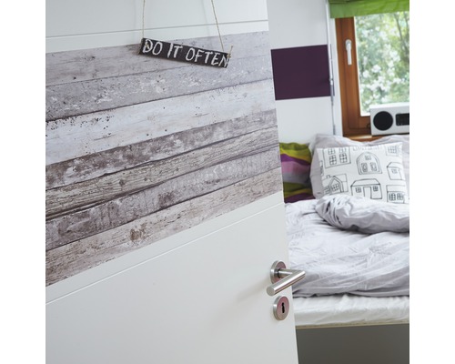 "Vue partielle d''une pièce avec une porte ouverte, décorée d''un papier peint imitation bois et portant un panneau indiquant ""Do it often""."