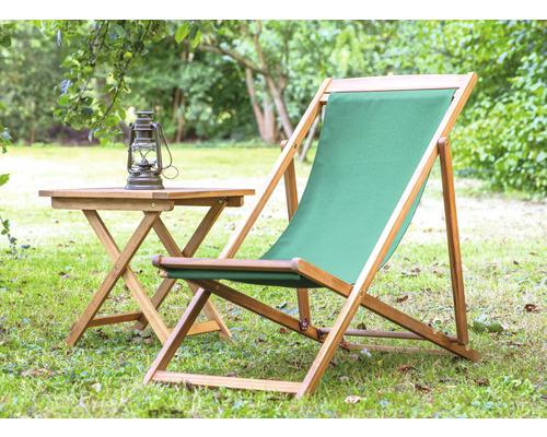 Gartenszene mit Klapptisch, Öllampe und Liegestuhl mit Holzrahmen und Stoffbezug