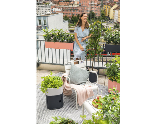 Balkonszene mit Frau, Stuhl, Pflanzgefässen und Blick auf die Stadt