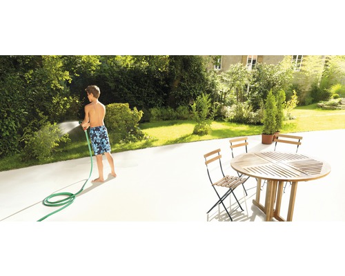 Junge giesst Pflanzen mit Gartenschlauch auf Terrasse mit Gartentisch und Gartenstühlen