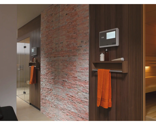Innenansicht einer Sauna mit Holzverkleidung, Handtuch, Steuerung und dekorativer Backsteinwand