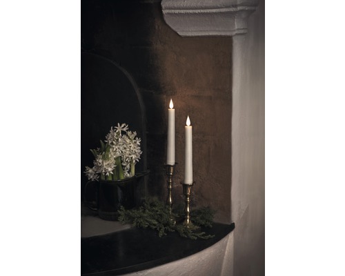 Arrangement décoratif avec bougies, fleurs et verdure sur une cheminée.