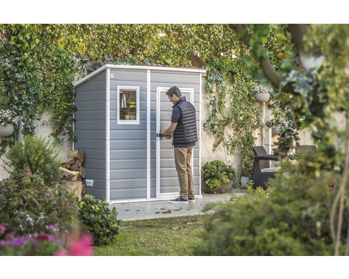 Gartenszene mit Geräteschuppen und einer Person, die die Tür öffnet