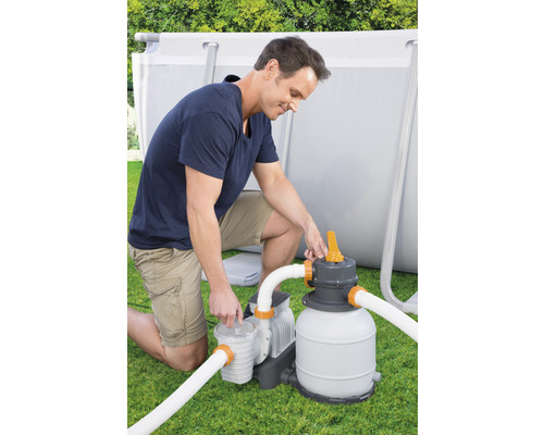 Un homme installe un système de filtration à sable pour une piscine dans le jardin.