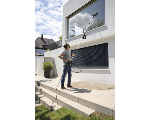 Une personne nettoie les vitres d''une maison moderne avec un nettoyeur haute pression et une lance télescopique.