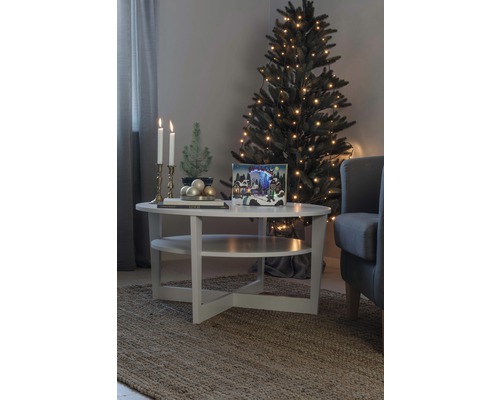 Weihnachtliche Wohnzimmerszene mit Tannenbaum, Lichtern und Dekorationen auf einem Tisch