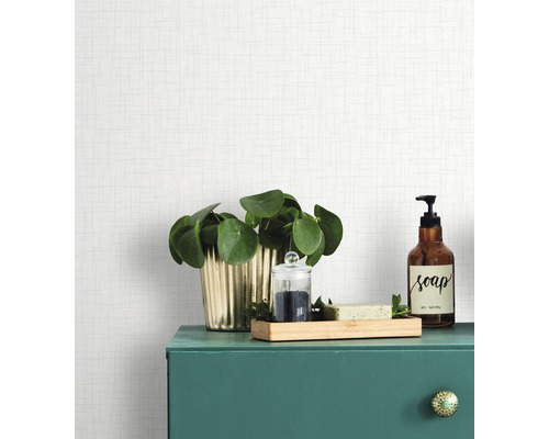 Objets de décoration sur un meuble de salle de bains vert devant un papier peint de couleur claire