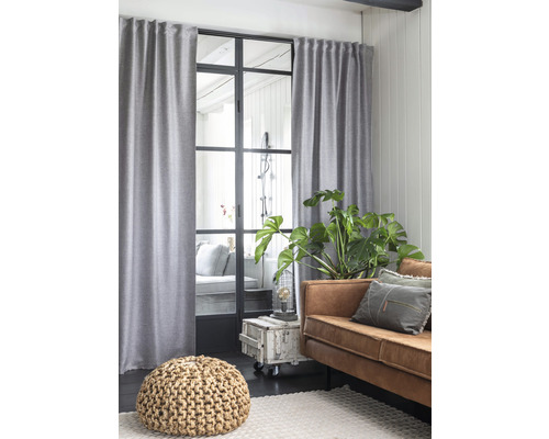 Wohnzimmer mit grauem Vorhang, Fenster mit Metallrahmen, braunem Sofa und Pouf