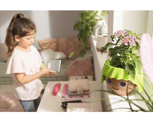 Fille avec un carnet à côté d''un pot de fleurs avec un visage dans une chambre d''enfant.