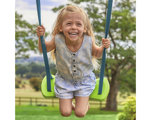 Une fillette souriante se balance sur une balançoire verte dans le jardin.