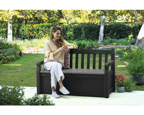Une femme assise sur un banc de jardin marron avec rangement dans le jardin.