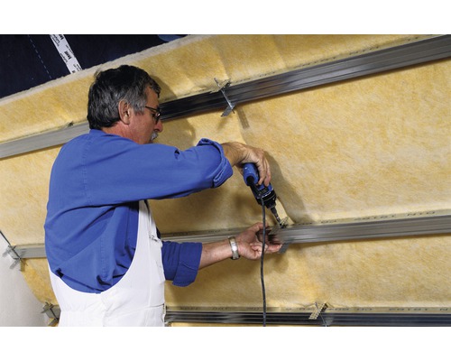 Un homme fixe de la laine isolante à une structure métallique à l''aide d''un tournevis. Isolation pour l''aménagement intérieur.