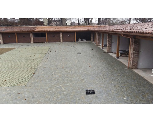 Vue extérieure d''une cour avec des pavés, des garages et des places de stationnement.