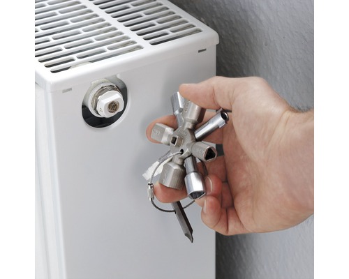 Eine Hand bedient einen Heizkörperentlüftungsschlüssel an einem Heizkörper.