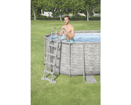 Un homme entre dans une piscine tubulaire dans le jardin à l''aide d''une échelle.