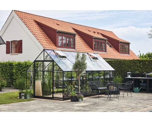 Gewächshaus mit Glaswänden und schwarzem Rahmen im Garten mit Gartenmöbeln