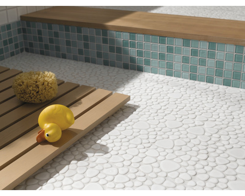 Salle de bains avec sol en galets, banc avec mosaïque et caillebotis en bois avec éponge de bain et canard en caoutchouc