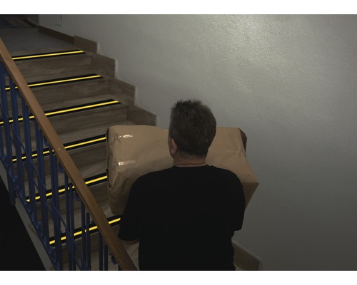 Homme portant un colis sur un escalier avec des bandes antidérapantes
