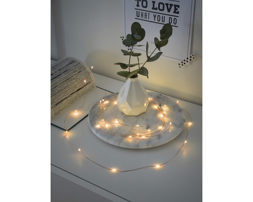 Guirlande lumineuse décorative avec de fines LED et fil de cuivre, disposée autour d''un vase sur une table