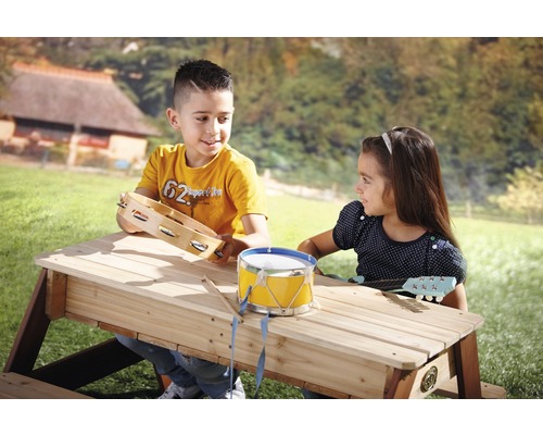 Zwei Kinder spielen an einem Picknicktisch im Freien mit Musikinstrumenten.