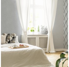 Helles Schlafzimmer mit Bett, Vorhängen und einer Wand mit Strukturtapete