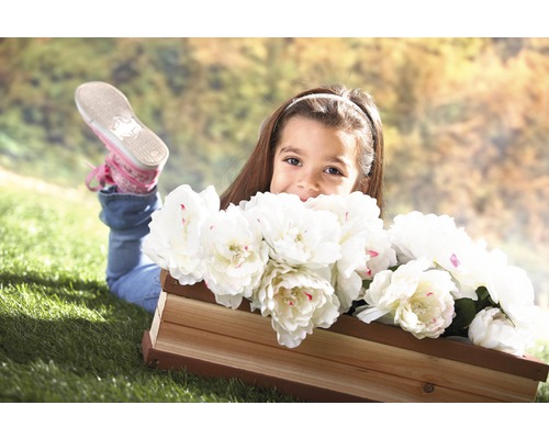 Ein Mädchen liegt mit einem Holzkasten voller weißer Blumen im Gras