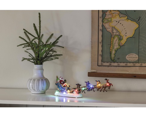 Scène décorative avec des branches de sapin dans un vase, une figurine de traîneau du Père Noël illuminée et une carte de l''Amérique du Sud.