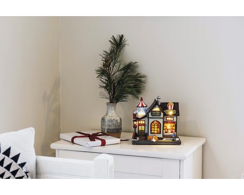 Dekorative Popcornfabrik als leuchtendes Deko-Element neben Geschenk und Vase mit Tannenzweigen auf einer Kommode