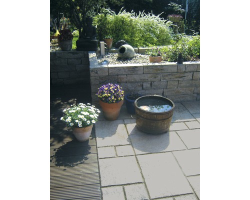 Dekorativer Garten mit Natursteinmauer, Buddhafigur, Pflanzen in Töpfen und einem Wasserfass