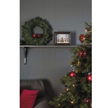 Salon décoré pour les fêtes avec sapin de Noël, couronne et décorations sur une étagère