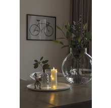 Arrangement décoratif avec vase, bougie et figurine sur une table, avec une image de vélo en arrière-plan.