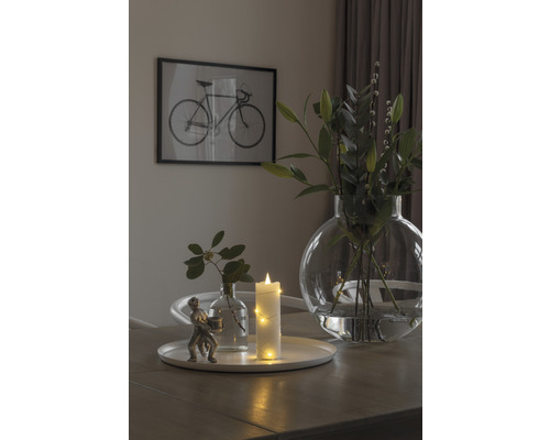 Arrangement décoratif avec vase, bougie et figurine sur une table, avec une image de vélo en arrière-plan.