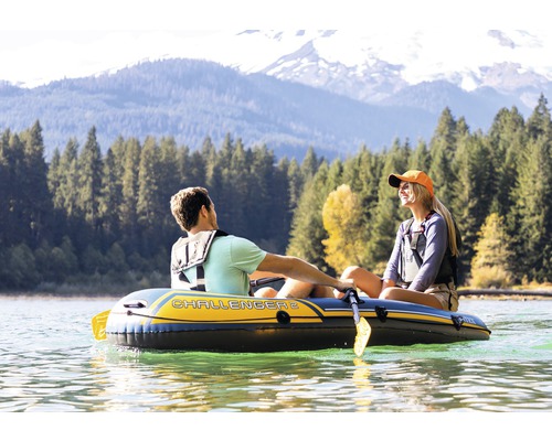Deux personnes dans un bateau pneumatique Challenger 2 sur un lac devant un paysage de montagne boisé.