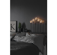 Dekorative Lampe mit fünf Glühbirnen auf einem Nachttisch im Schlafzimmer.