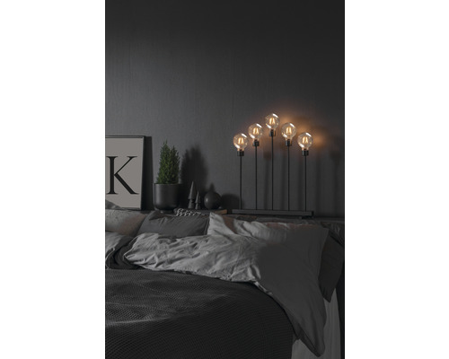 Dekorative Lampe mit fünf Glühbirnen auf einem Nachttisch im Schlafzimmer.